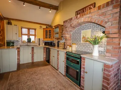 a large kitchen with white cabinets and a brick wall at The Old Dairy in Shrewsbury