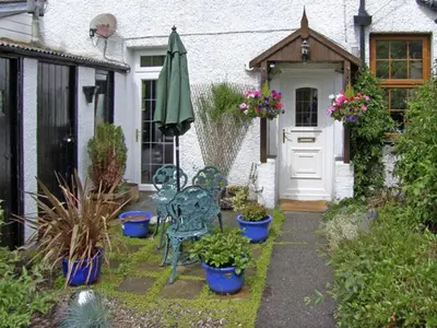 a garden with a door and chairs and plants at Railway Cottage in Fairbourne
