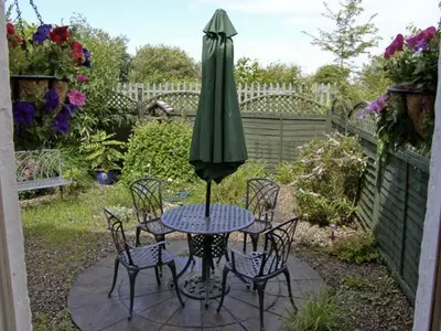 a table and chairs with a green umbrella on a patio at Railway Cottage in Fairbourne