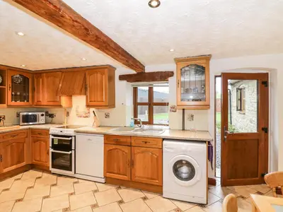 a kitchen with wooden cabinets and a washer and dryer at The Stable in Craven Arms
