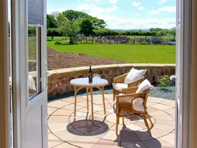 a patio with a table and chairs and a bottle of wine at Byre Cottage in Nesscliffe