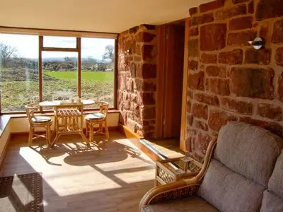 a living room with a stone wall and a table and chairs at Byre Cottage in Nesscliffe