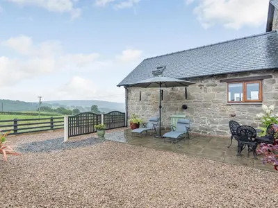 a stone cottage with a patio with chairs and an umbrella at The Granary in Llanfair Caereinion