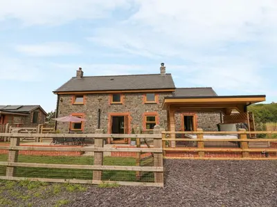 a stone house with a wooden fence in front of it at The Farmhouse in Capel Bangor
