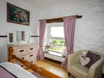 a bedroom with a bed and a window with a chair at Hendy Cottage in Llanbedr