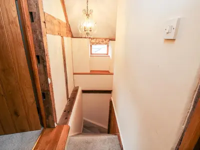 a hallway with a staircase and a chandelier at The Old Farmhouse in Craven Arms