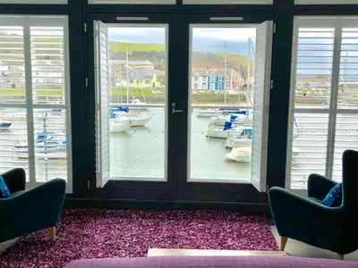 a room with two chairs and windows with boats in the water at Harbourmaster Hotel in Aberaeron