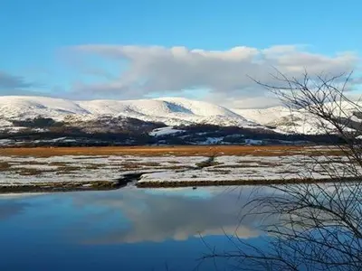 a reflection of snow covered mountains in a body of water at Bwlcheinion Sea View Glamping in Machynlleth