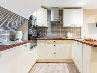 a kitchen with white cabinets and a wooden floor at Ty Bach Twt in Dyffryn