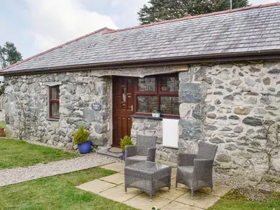 a stone cottage with two chairs and a door at Bwthyn Clyd in Dyffryn