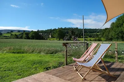 two chairs sitting on a deck under an umbrella at Wye Glamping in Velindre