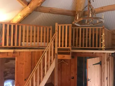 an attic room with wooden stairs and a chandelier at Coed y Marchog Woodland Retreat in Hereford