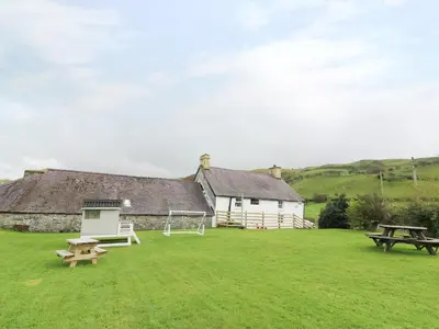 a house with a picnic table and benches in the grass at Penglanowen Fawr in Rhostie