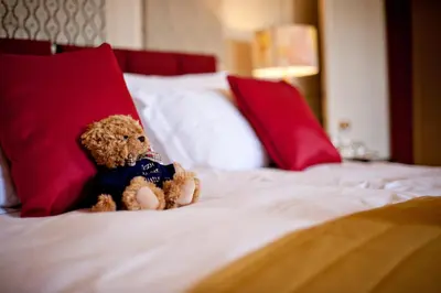 a teddy bear sitting on a bed with red pillows at Plas Nanteos Mansion in Aberystwyth