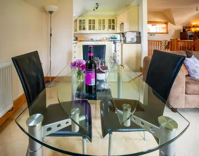 a glass table with two chairs and a bottle of wine at Berries Coach House in Church Stretton
