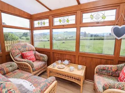 a living room with chairs and a table and windows at Tegfan in Rhayader