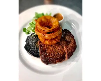 a white plate with a steak with onion rings on it at Seabreeze Restaurant With Rooms in Aberdyfi