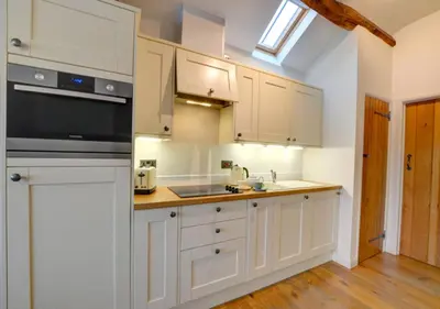 a kitchen with white cabinets and a sink at Smithy Cottage in Berriew