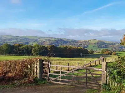 a wooden gate in a field with hills in the background at Green Lane Cottage in Newtown
