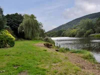 a grassy field next to a river with trees at Edw Lodge in Aberedw