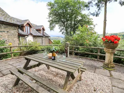 a wooden picnic table with a vase of red flowers at Cedar Cottage in Llanidloes