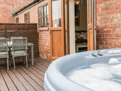 a tub on a deck with a table and chairs at Old Hall Barn 1 in Church Stretton