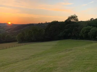 a green field with the sunset in the background at Llwyn Llwyd Cottage in Brecon
