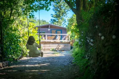a woman sitting on a swing in front of a house at Little Kestrel Cabin in Pennal