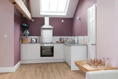 a kitchen with white cabinets and purple walls at The Hayloft, Wall End Farm in Leominster