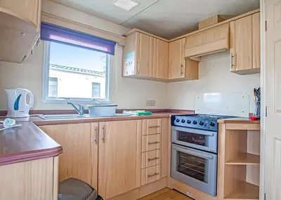 a kitchen with wooden cabinets and a stove top oven at The Village Holiday Park in New Quay
