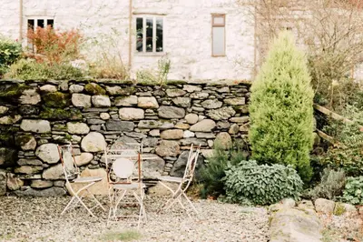 two chairs and a stone wall in front of a house at The Barn at Ty Beic in Bala