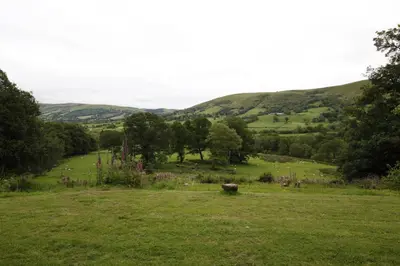 a field of grass with trees and hills in the background at Plas Esgair in Llanbrynmair