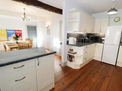 a kitchen with white cabinets and a wooden floor at Goronwy Cottage in Barmouth