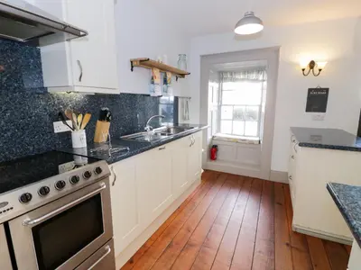 a kitchen with white cabinets and a wooden floor at Goronwy Cottage in Barmouth