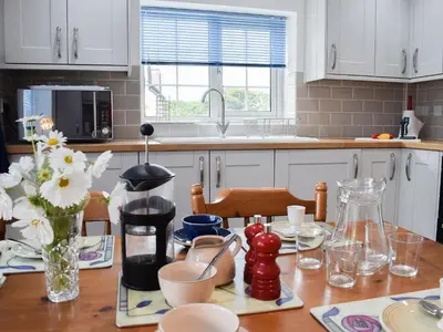 a kitchen with white cabinets and a wooden table at Glasfor in Llanon