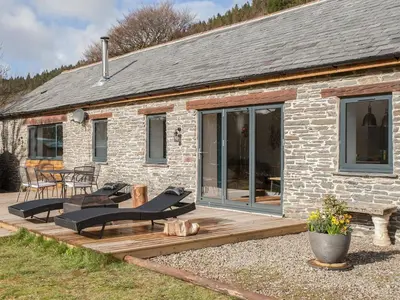 a brick house with a deck and chairs in front of it at The Pendre Longbarn in Pentre-briwnant