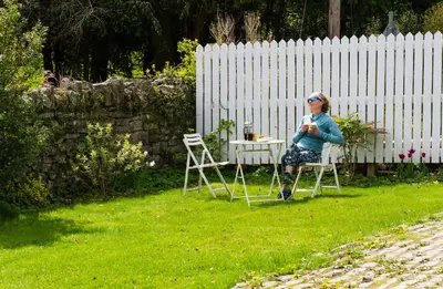a woman sitting on a chair in a yard at Station Cottage in Bucknell