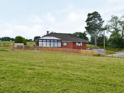 a red house with a fence and a grass field at Bryn Villa in Newbridge on Wye