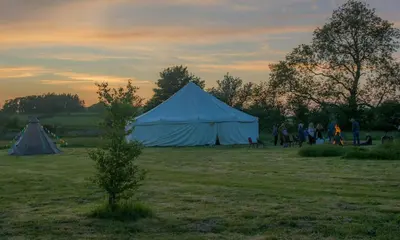 a group of people standing in a field with tents at The Rose Barn, Ysgubor y Rhosyn in Llandysul