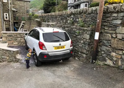 a little boy standing next to a car parked next to a stone wall at 3 Park View in Barmouth