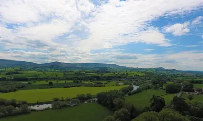 an aerial view of a green field with mountains in the background at Glanhenwye Courtyard Cottages in Glasbury