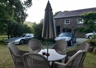 a table with chairs and an umbrella and some cars at The Mews, Talley in Llandeilo