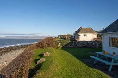 a house with a picnic table next to the ocean at Allt y Mor in Harlech
