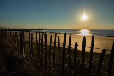 a fence on a beach with the sun setting at Allt y Mor in Harlech