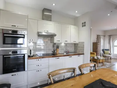 a kitchen with white cabinets and a wooden table at Harlech Apartments - Gwern in Harlech