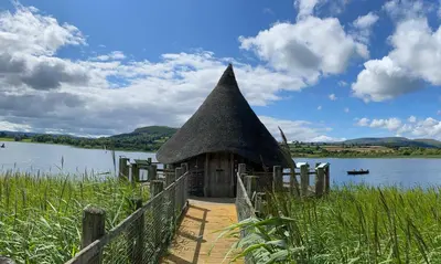 a building with a thatched roof next to a lake at Tegfan Garden Suite in Talgarth
