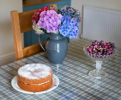 a table with a cake and a vase with flowers at Magnolia Cottage in Church Stretton