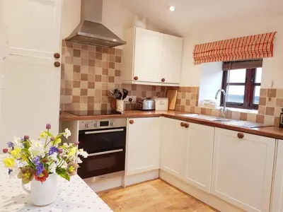 a kitchen with white cabinets and a vase of flowers on a table at River Cottage@Cwm Mill - Riverside Family Holidays in the Black Mountains in Hereford
