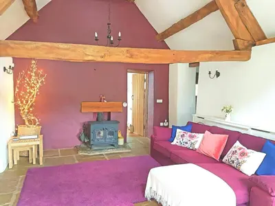 a living room with a purple couch and a wood stove at Old Bake House Cottage @ Cwm Mill in Michaelchurch Escley