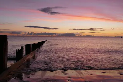 a pier on the beach with a sunset in the background at Bae Abermaw Hotel in Barmouth